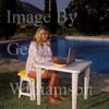 GW25470-50 = Young lady using laptop computer and mobile telephone by the side of the swimming pool of a country finca, Mallorca, Balearic Islands, Spain.